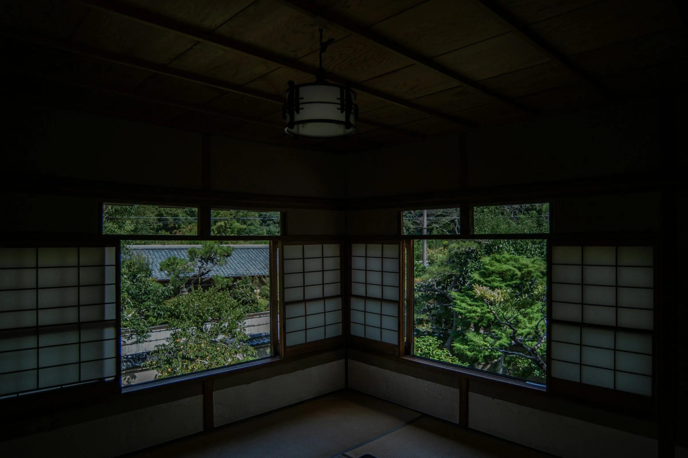 A corner of a tatami room with shoji windows opening onto green trees
