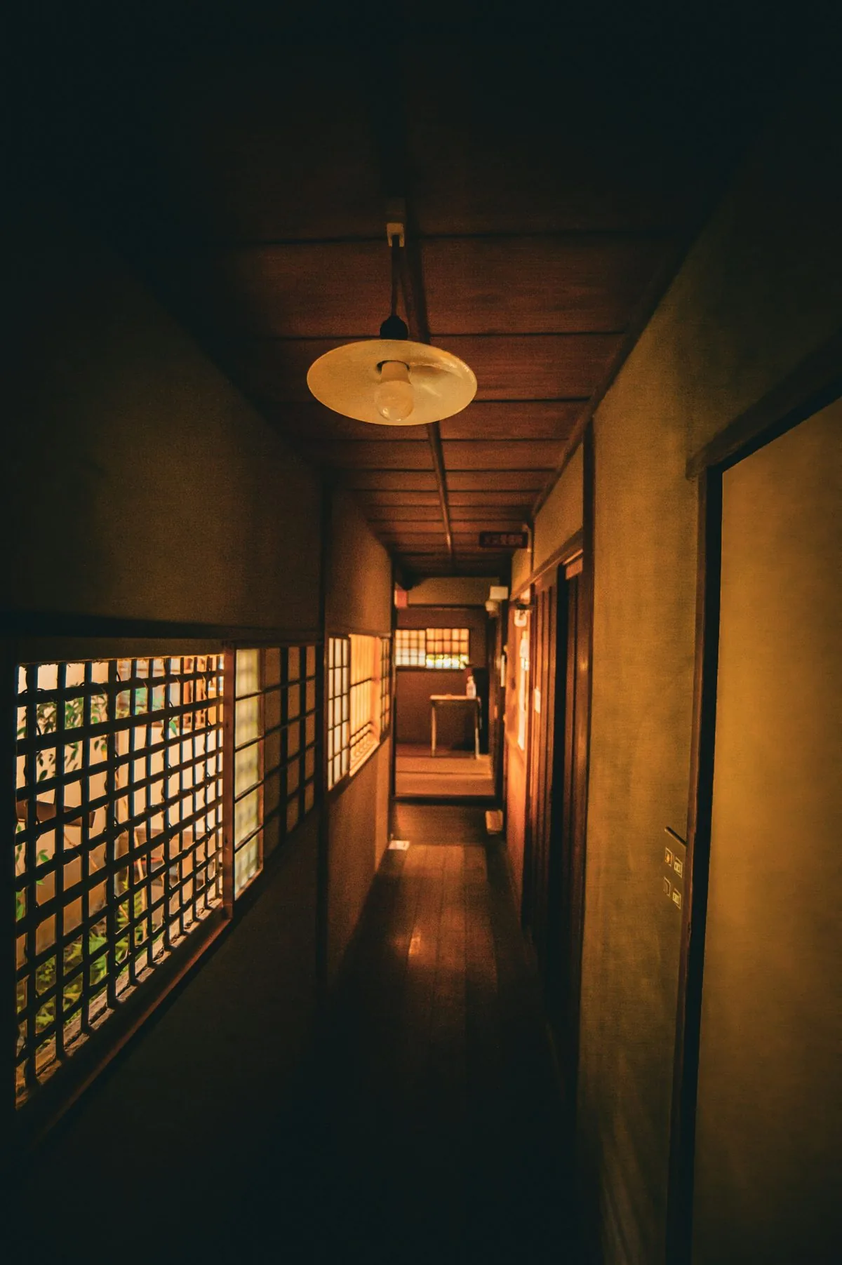 A dim corridor with lattice windows and a hanging paper lantern