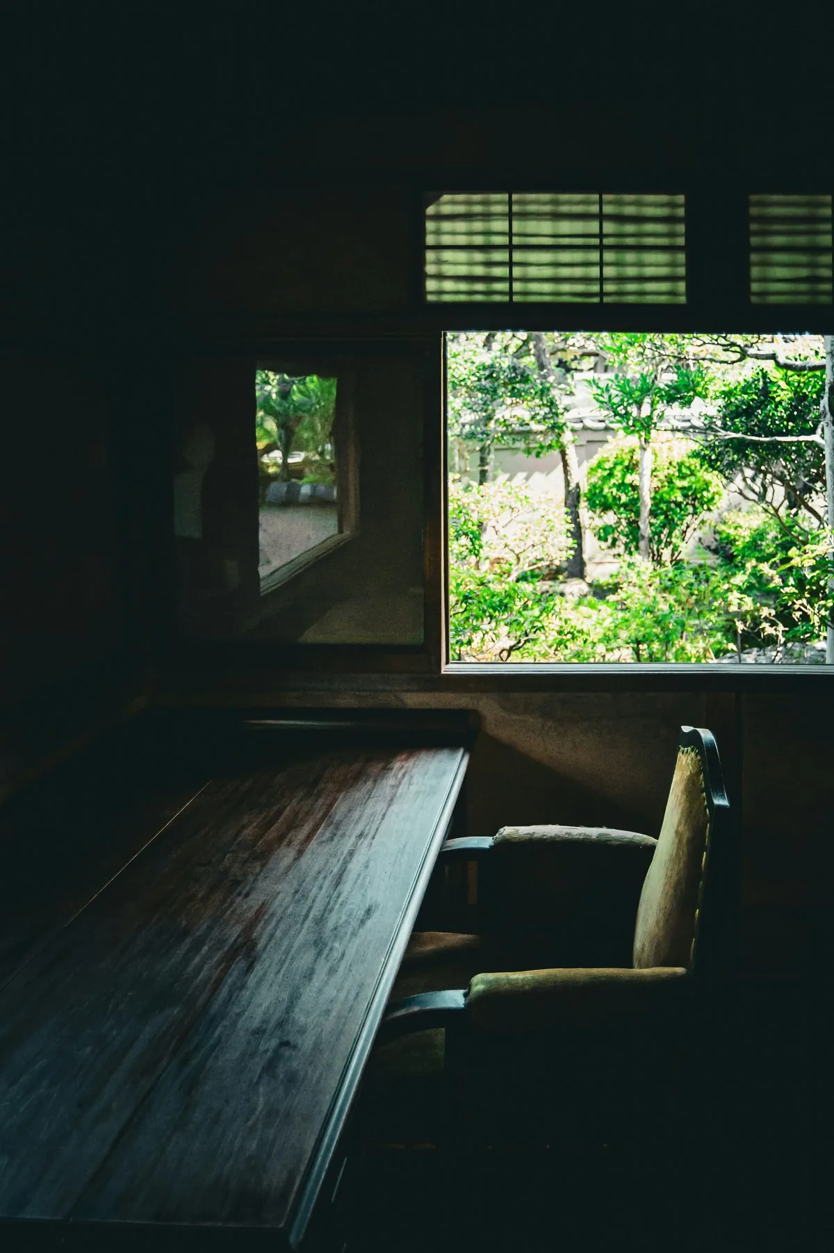 A wooden desk and chair by a window onto the garden