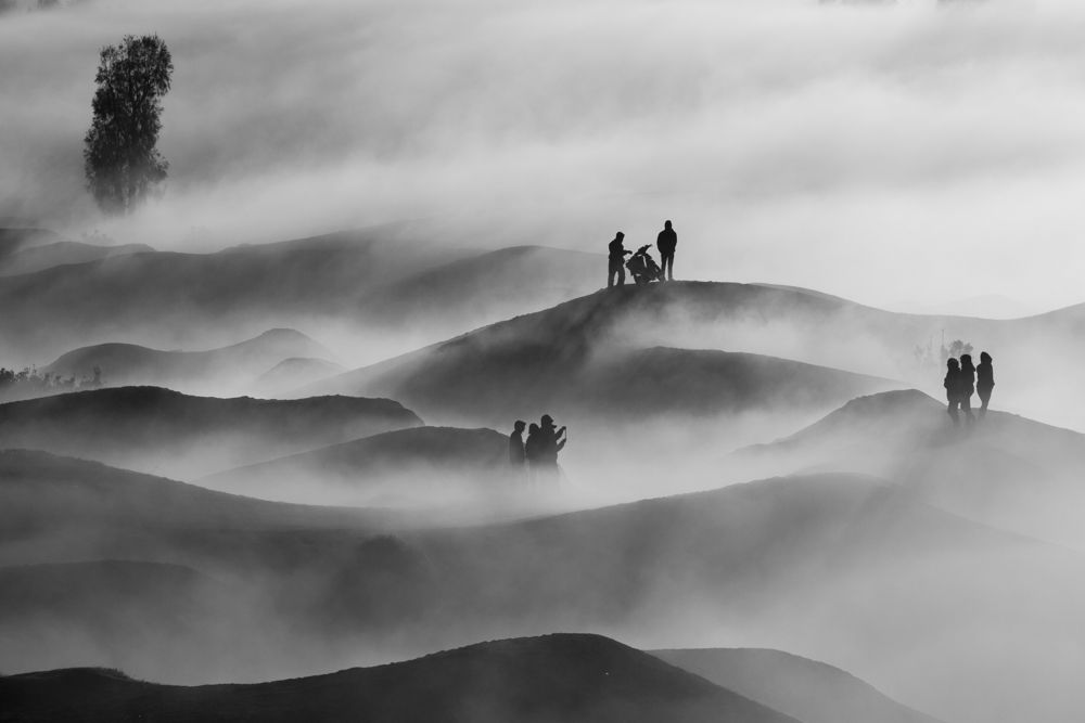 Black and white hills drowned in fog with small figures standing on the ridges