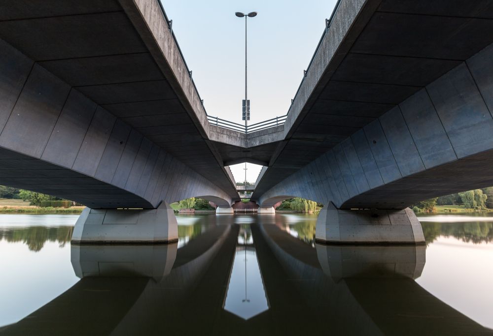 The underside of two concrete bridges mirrored in still water