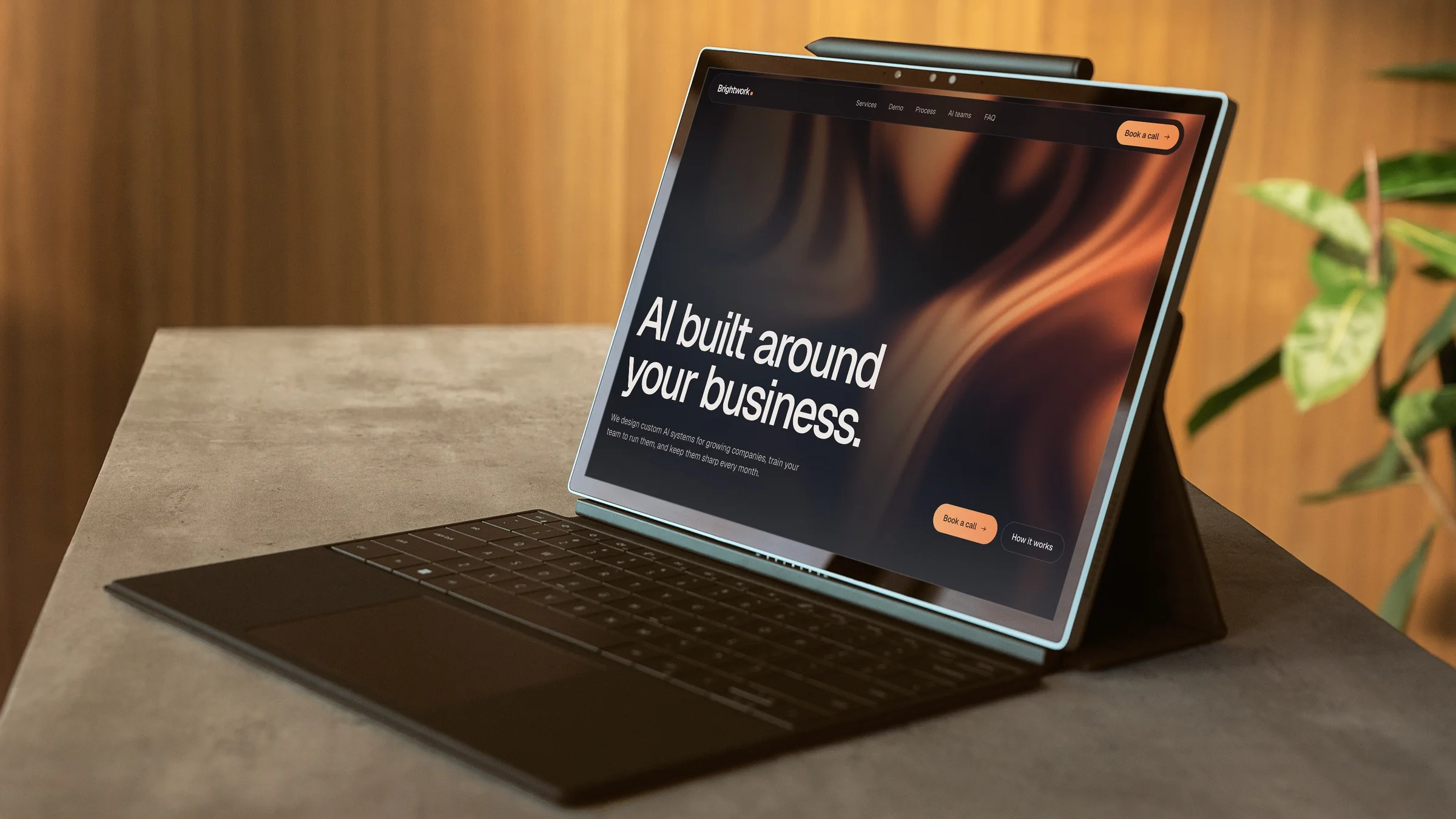 Brightwork homepage on a tablet laptop: the headline AI built around your business. over an orange gradient, on a stone desk by a wood slat wall
